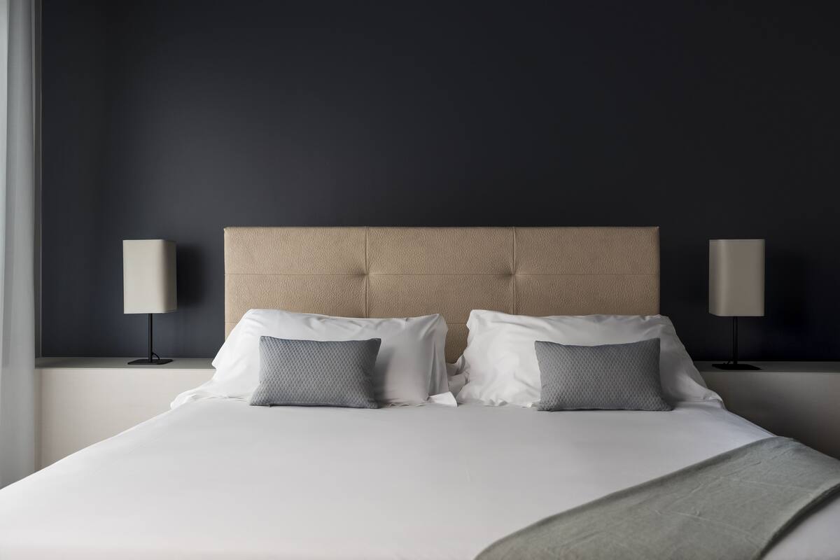 A neatly made bed with a tufted headboard, two bedside lamps, and a grey throw blanket.