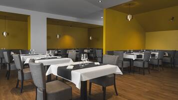 Un restaurante con varias mesas y sillas, piso de madera e iluminación colgante.