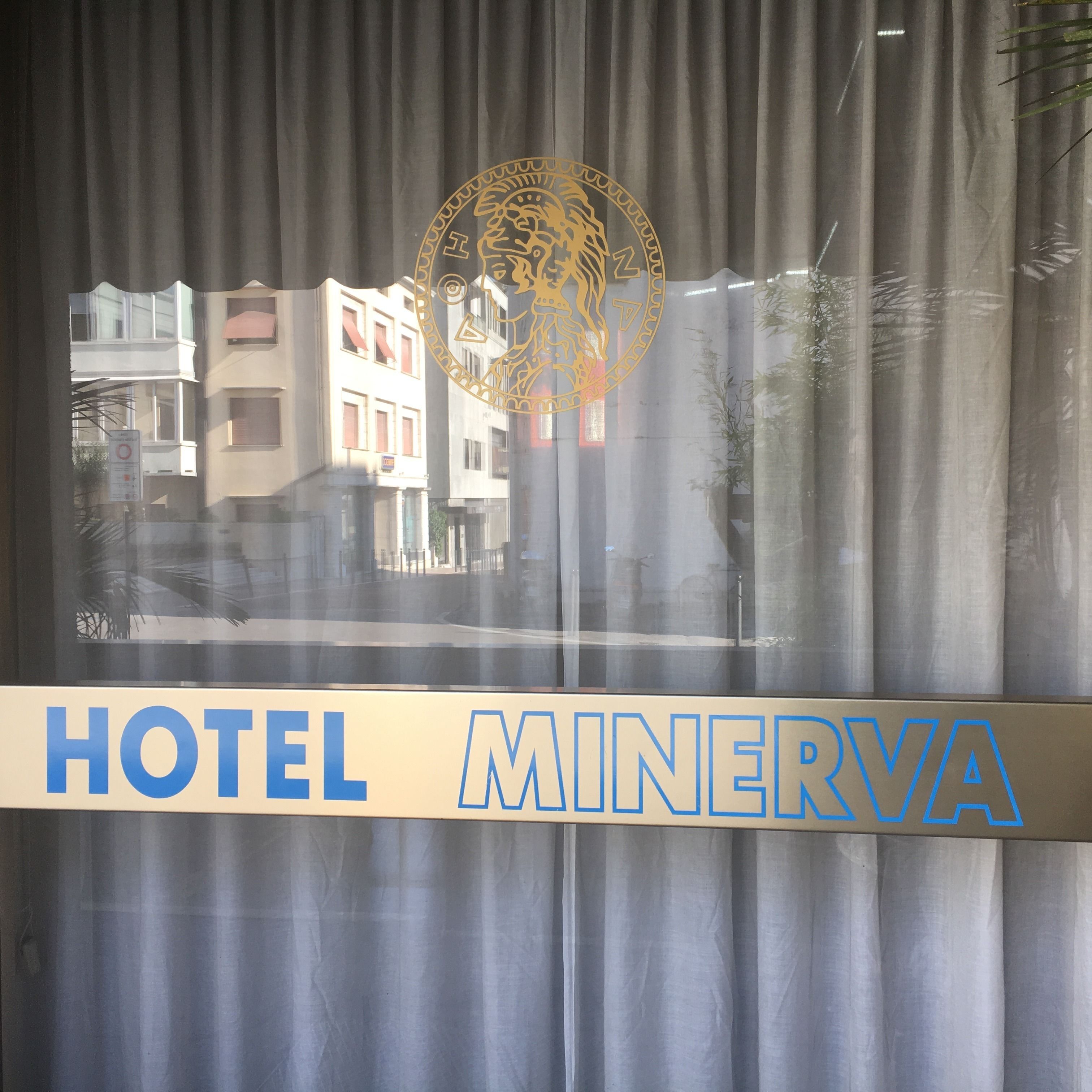 Segnaletica di un hotel con la scritta "HOTEL MINERVA" in caratteri blu su sfondo beige.