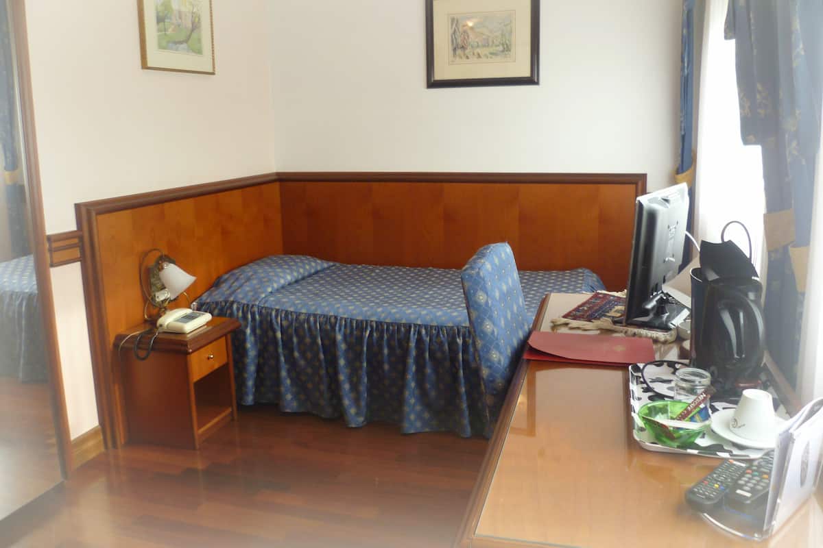 A small hotel room with a single bed, a desk with a computer, a telephone, and a coffee maker.