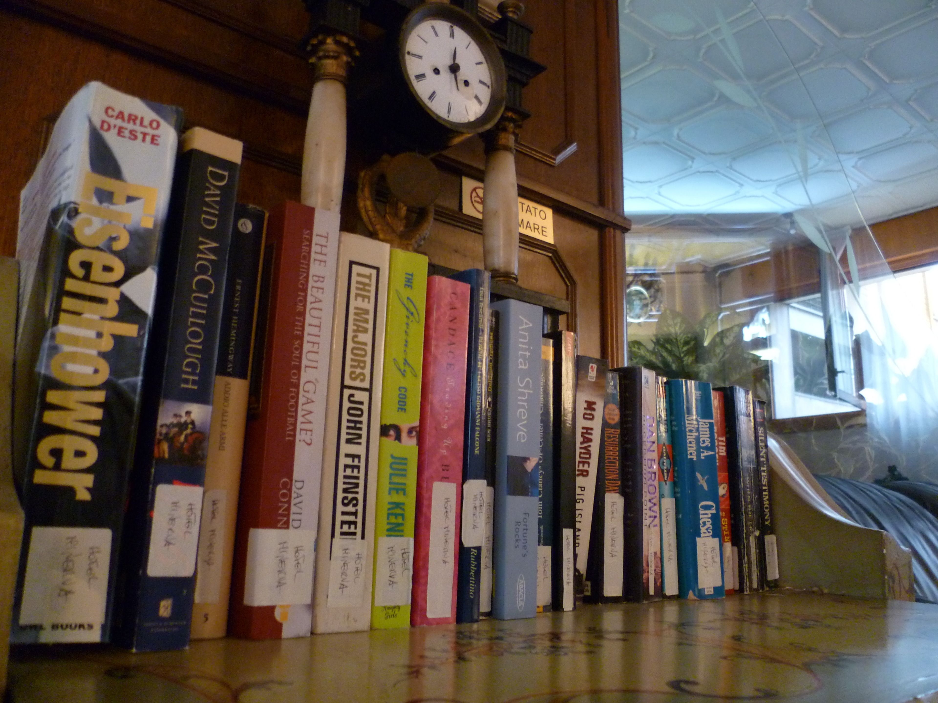 A bookshelf with various books, a clock, and a sign that reads "TATTOO MARE".
