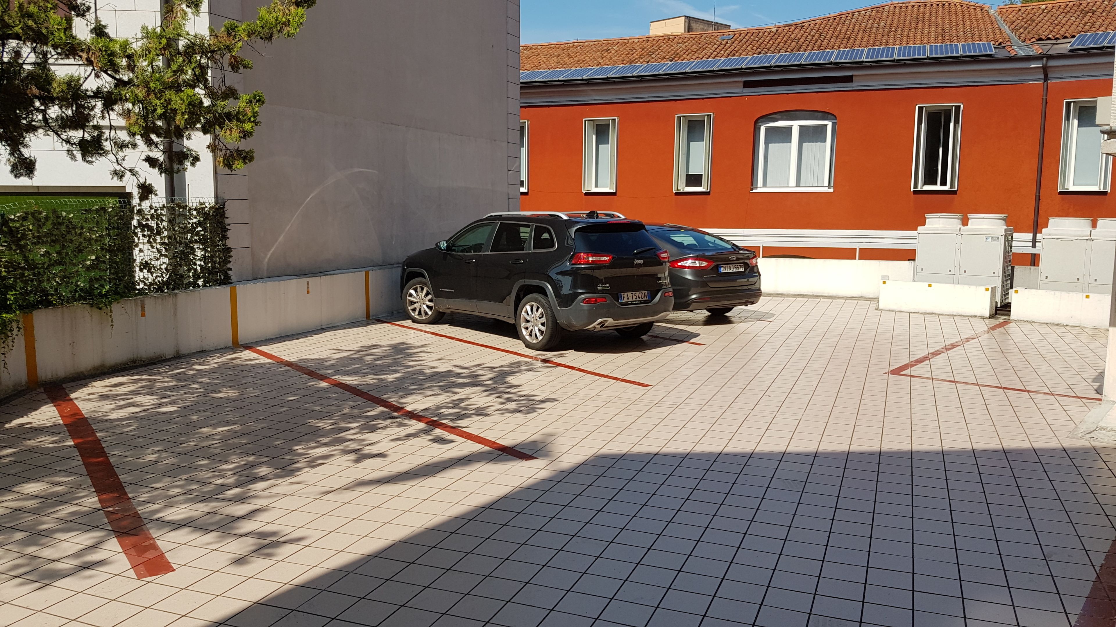Un espace de stationnement avec deux voitures, un bâtiment à l’extérieur rouge et blanc, et un arbre aux feuilles vertes.