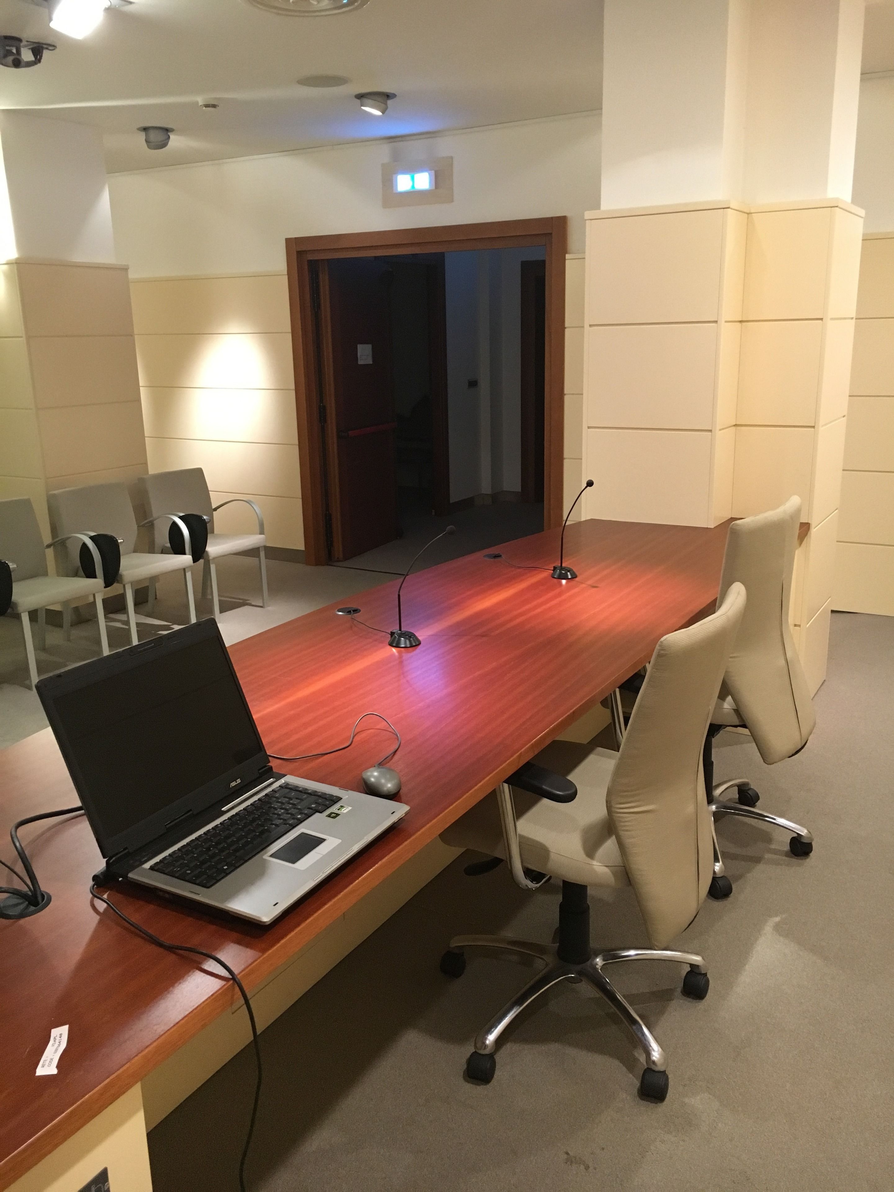 Un salón de conferencias con una larga mesa de madera, cuatro sillas, una computadora portátil y un micrófono.