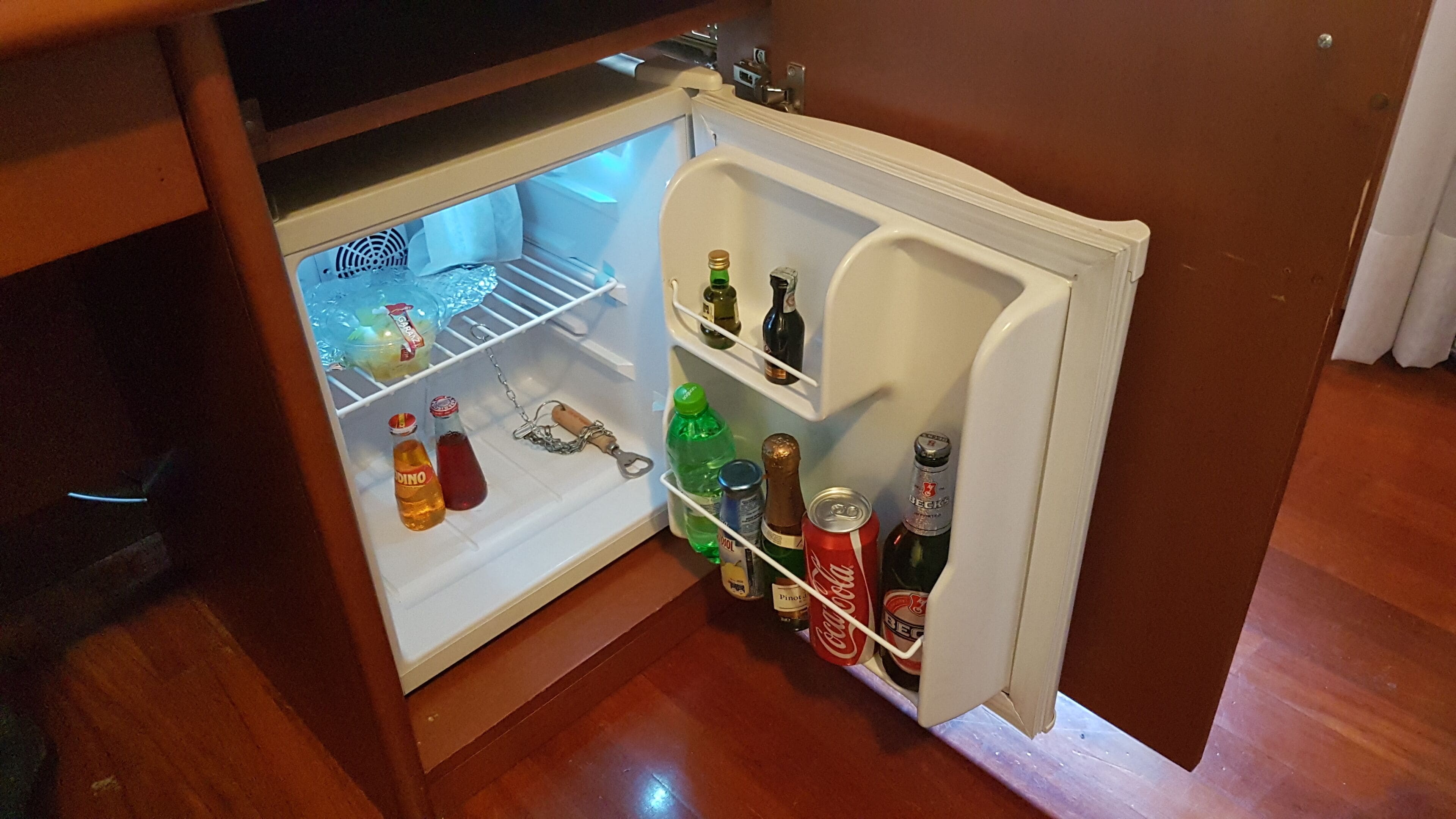 A small refrigerator with shelves containing various beverages and a bottle of Coca-Cola.