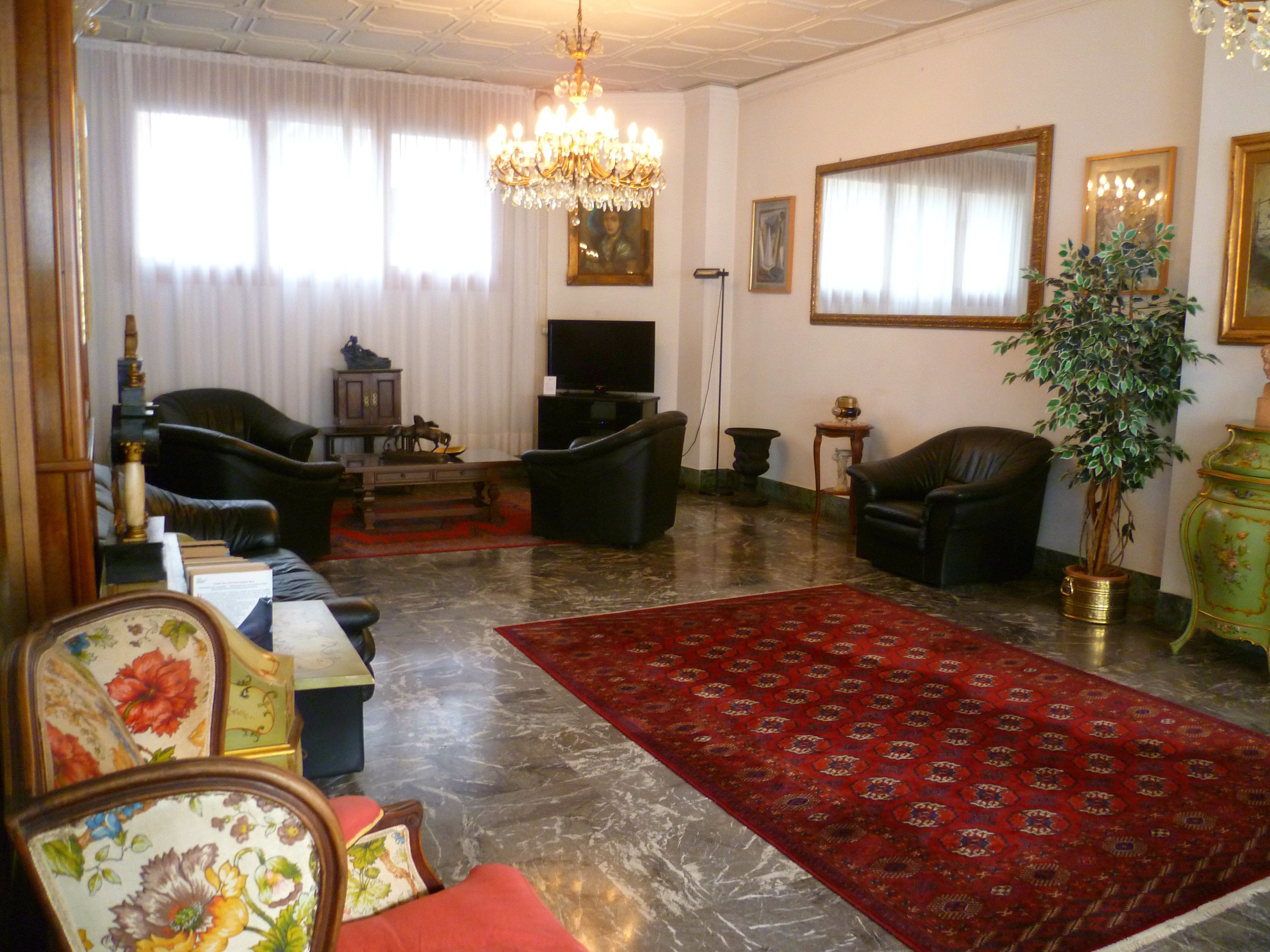 Un salón con candelabro, dos sofás de cuero, un tapete rojo estampado y una televisión.