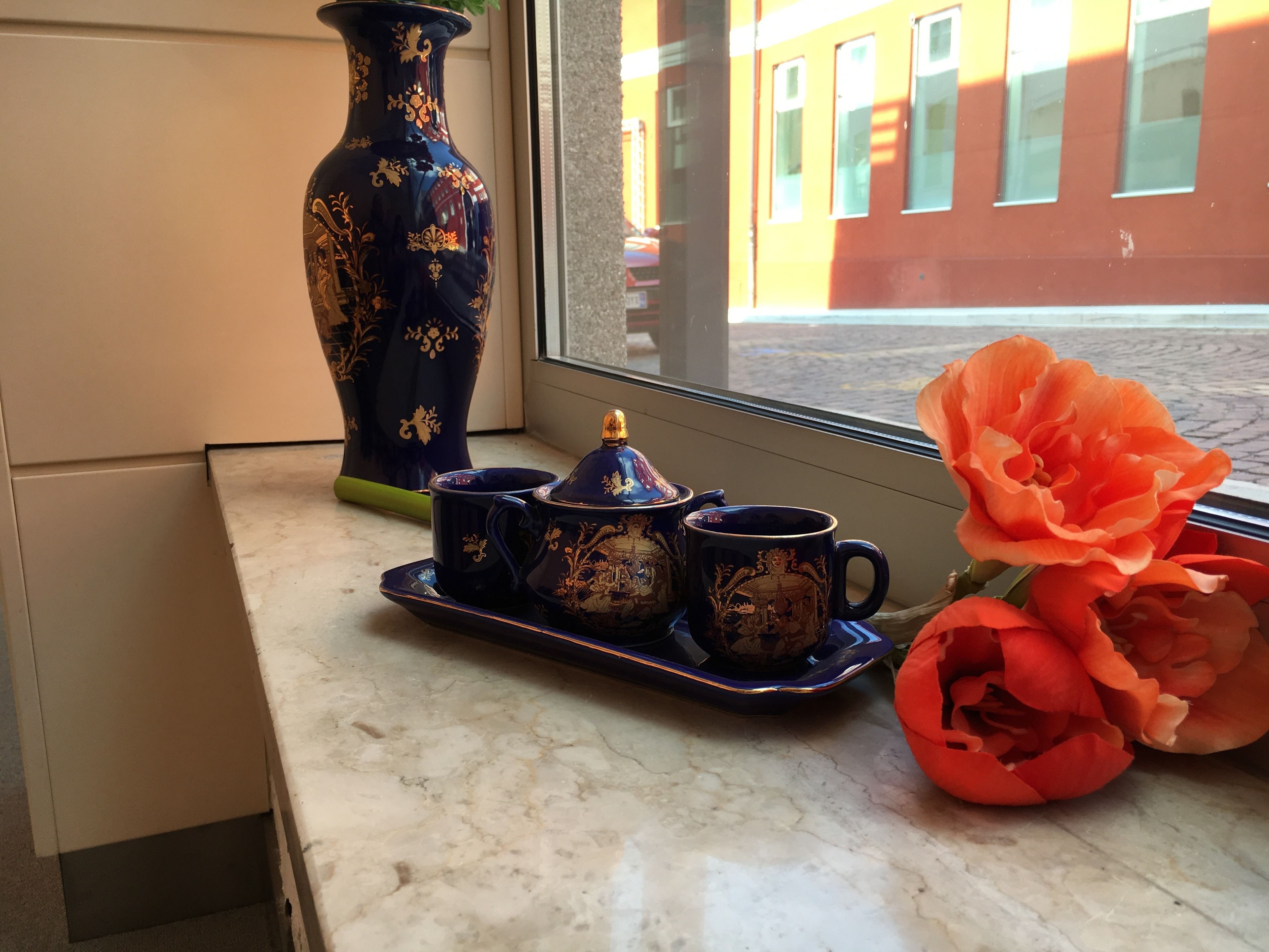A table with a tea set and a vase of flowers by a window.