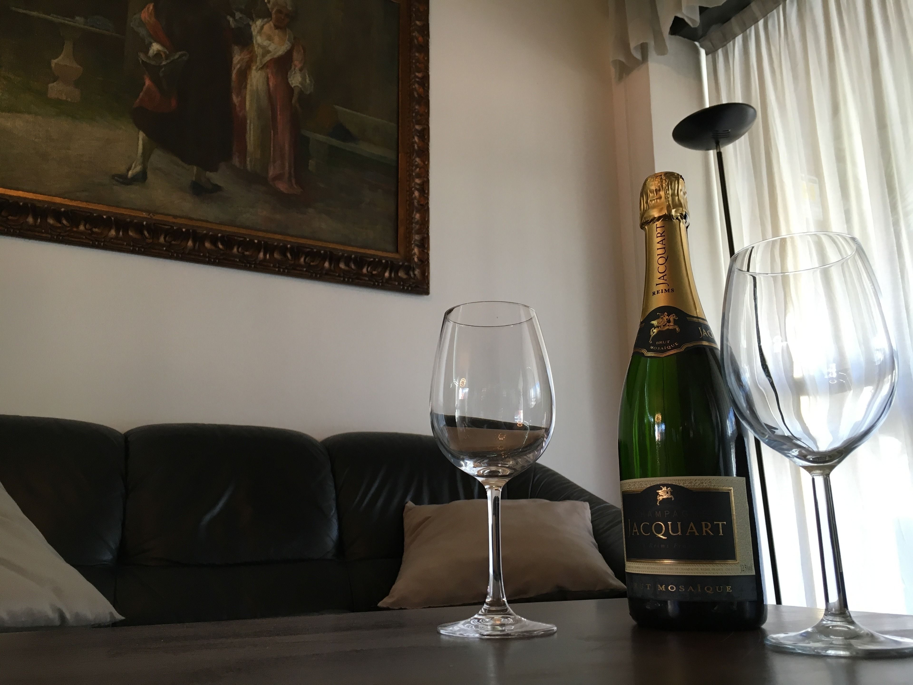 A living room with a dark leather sofa, a wine glass, and a bottle of champagne on a table.