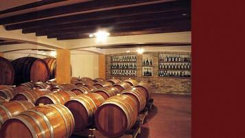 A wine cellar with wooden barrels and shelves of wine bottles.