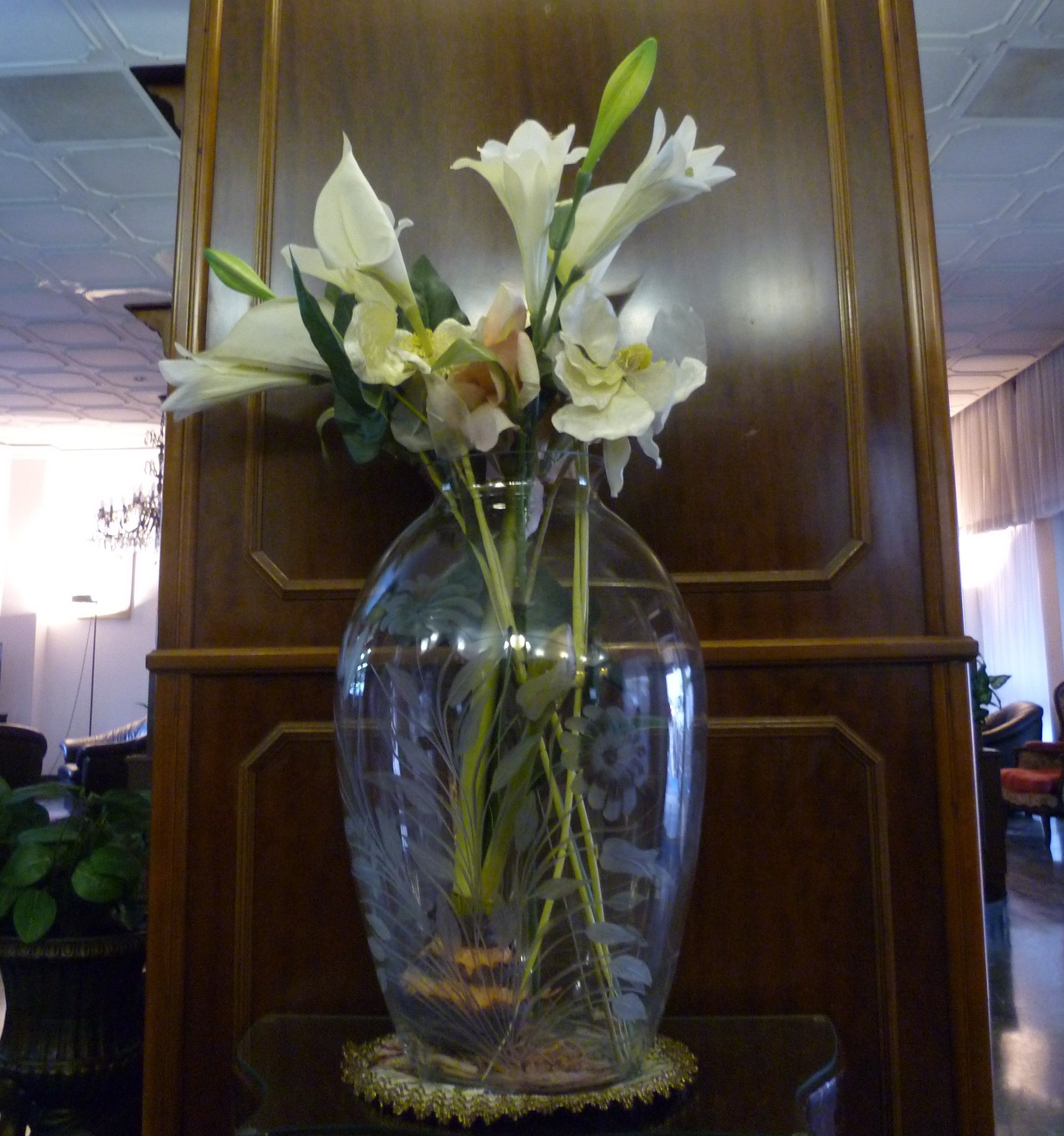 A clear glass vase with white flowers on a wooden pedestal.