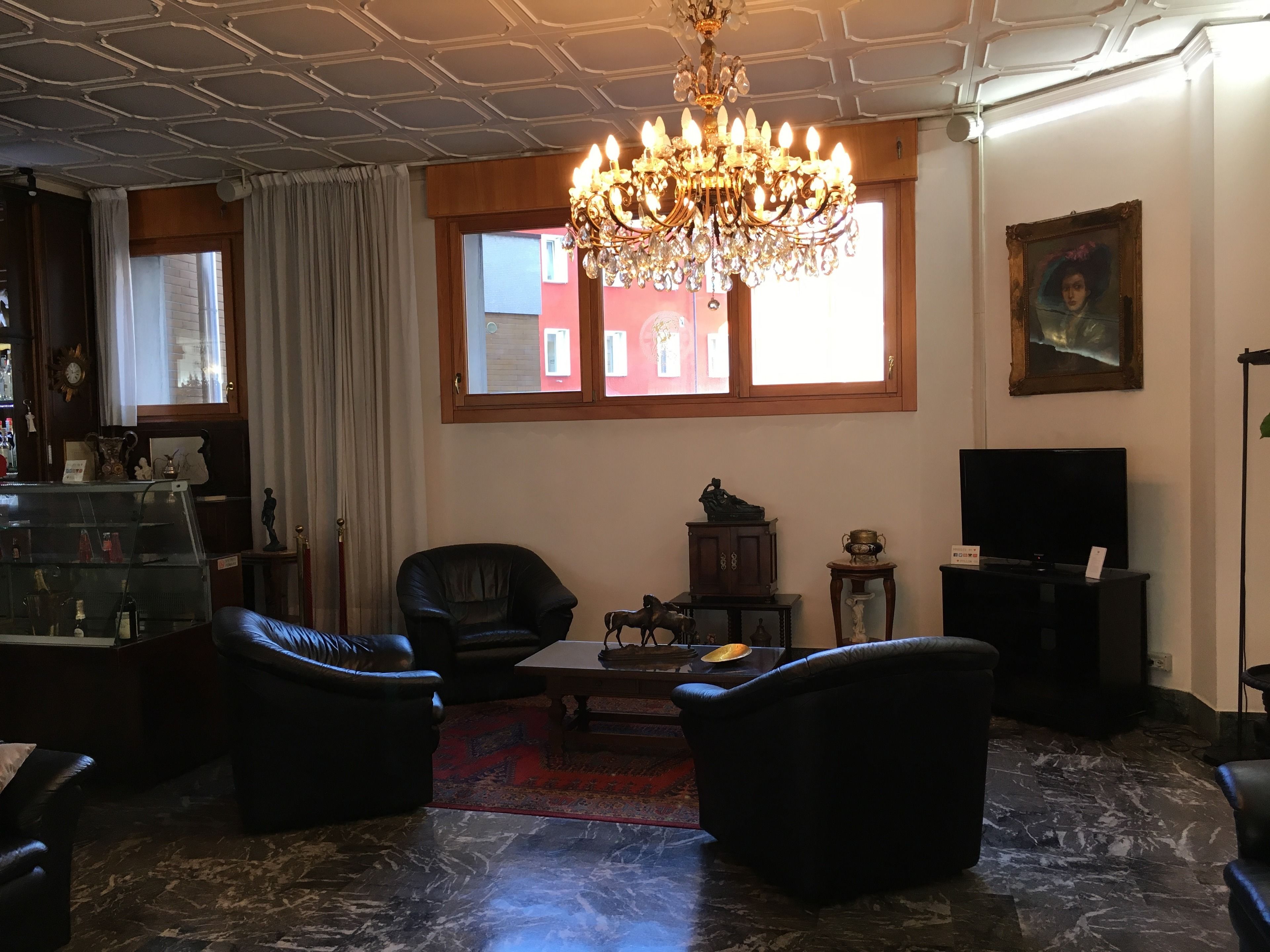 Uma sala de estar com um candelabro, sofás de couro, uma televisão e um tapete vermelho estampado.