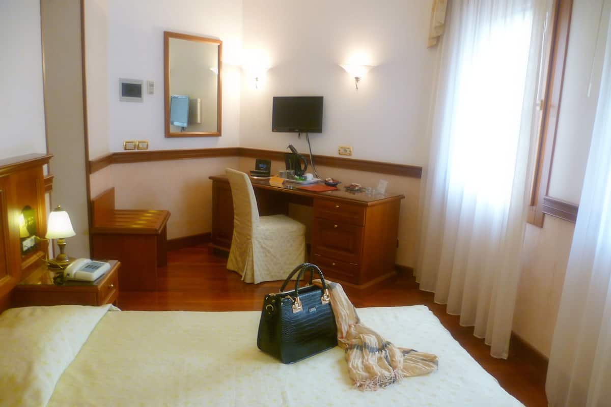 A hotel room with a bed, a desk, a chair, a television, and a lamp.