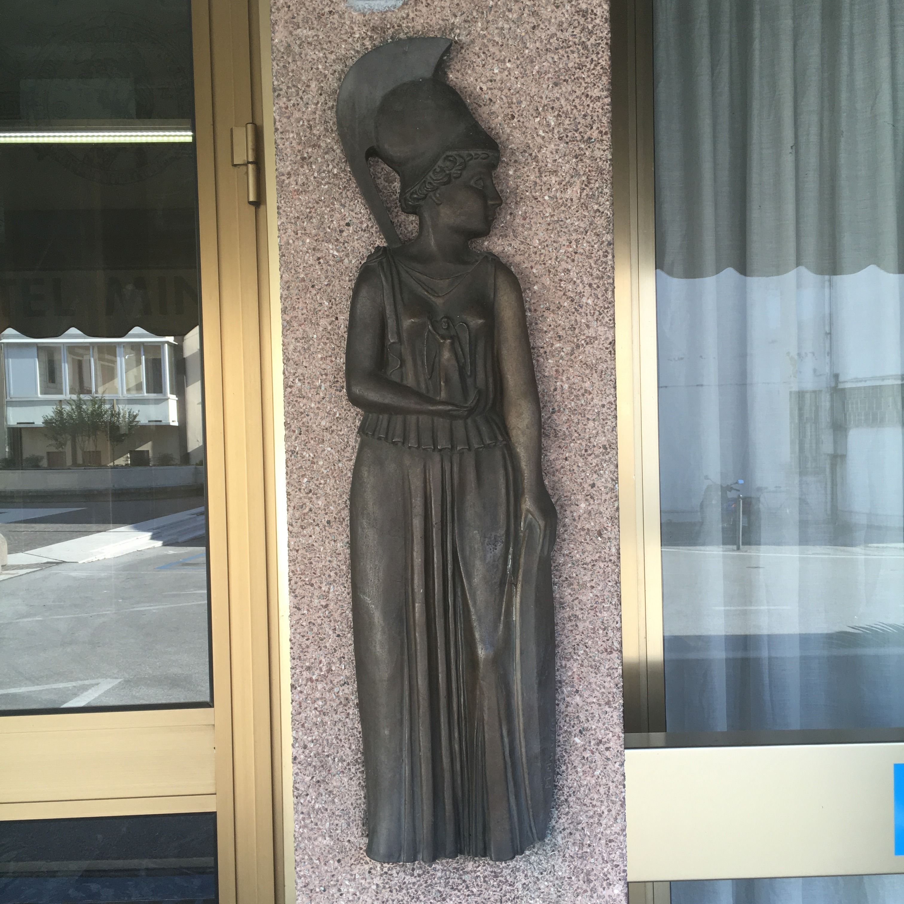 Eine Statue einer Frau in Kleid und Hut, die an einer strukturierten Wand angebracht ist.