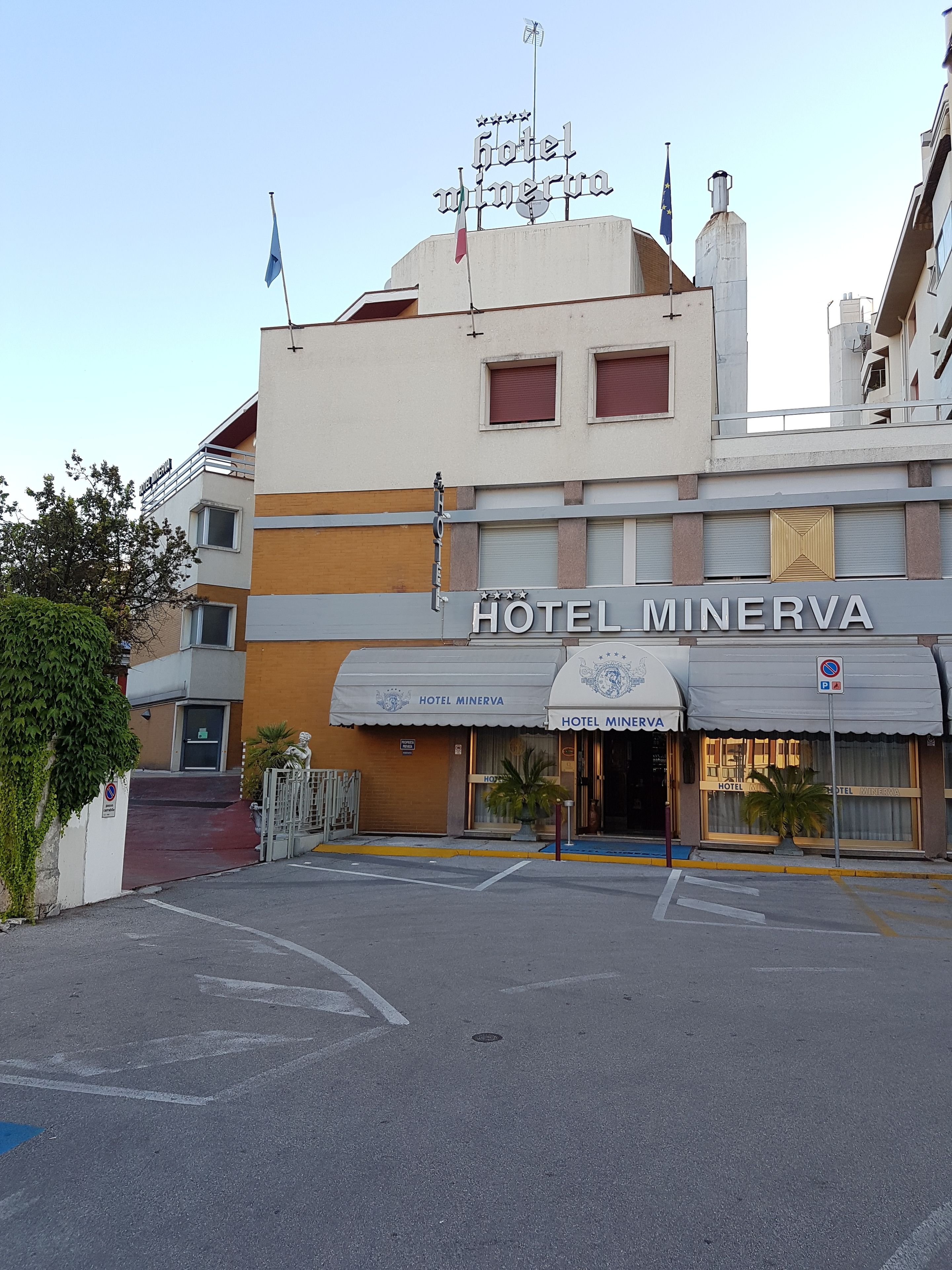 A hotel named Hotel Minerva with a modern facade, a prominent entrance, and a flag on top.