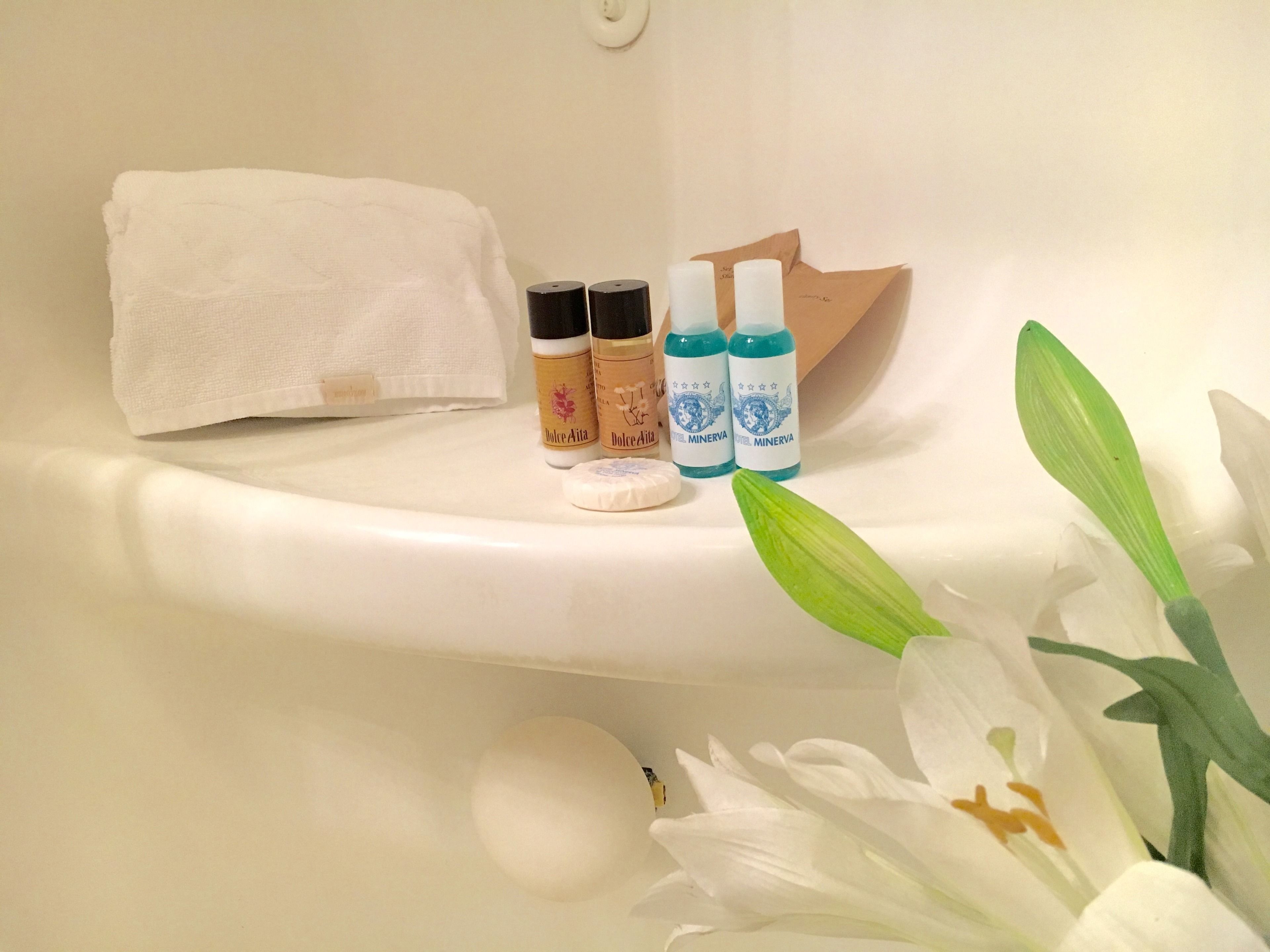 A bathroom with a white bathtub, a white towel, and two bottles of Dolce Aita and Dolce Minerva bath products.