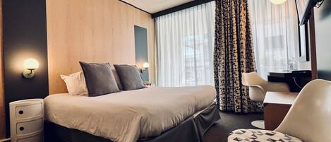 A modern hotel room with a large bed, a desk, and a chair. There are two bedside tables and a lamp on each.