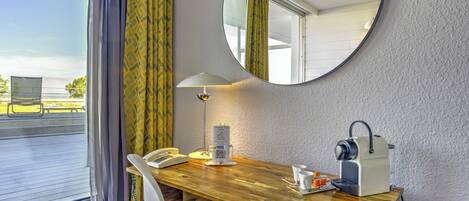 A hotel room with a wooden desk, a telephone, a coffee maker, and a mirror on the wall.