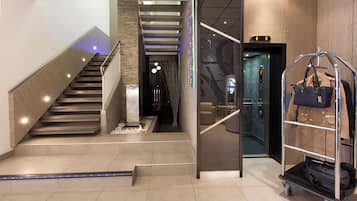 A modern hotel lobby with a staircase, a luggage cart, and a reception area.