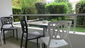 Een balkon met een tafel en stoelen, omringd door groen en een witte balustrade.