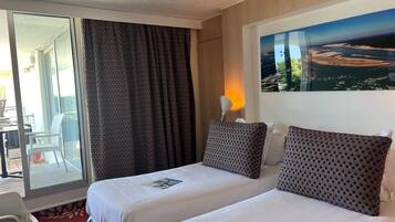A hotel room with two beds, a large window with curtains, a painting on the wall, and a view of the outdoors.