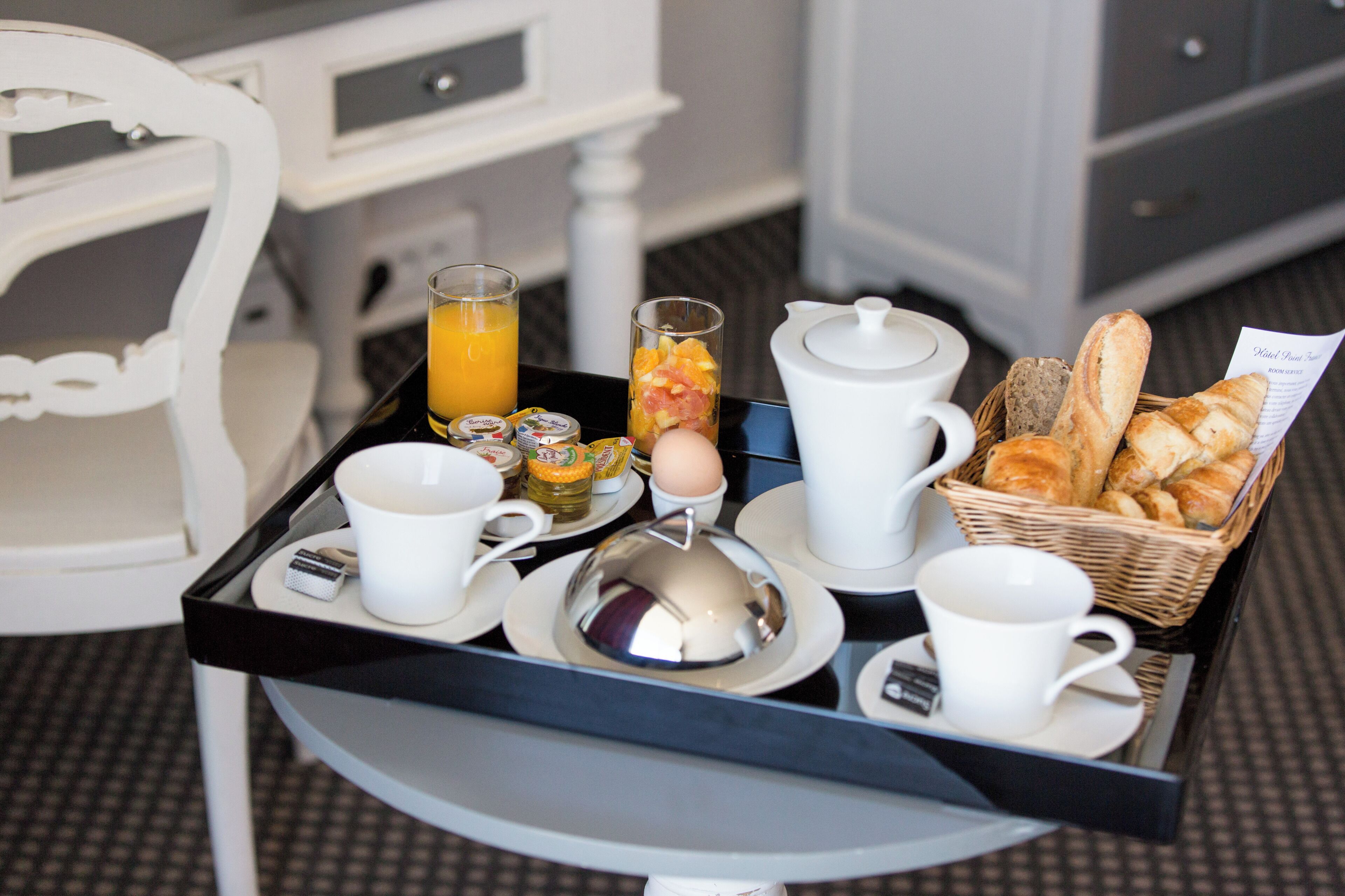 A breakfast tray with croissants, a teapot, a cup, a glass of orange juice, and a small container of eggs.
