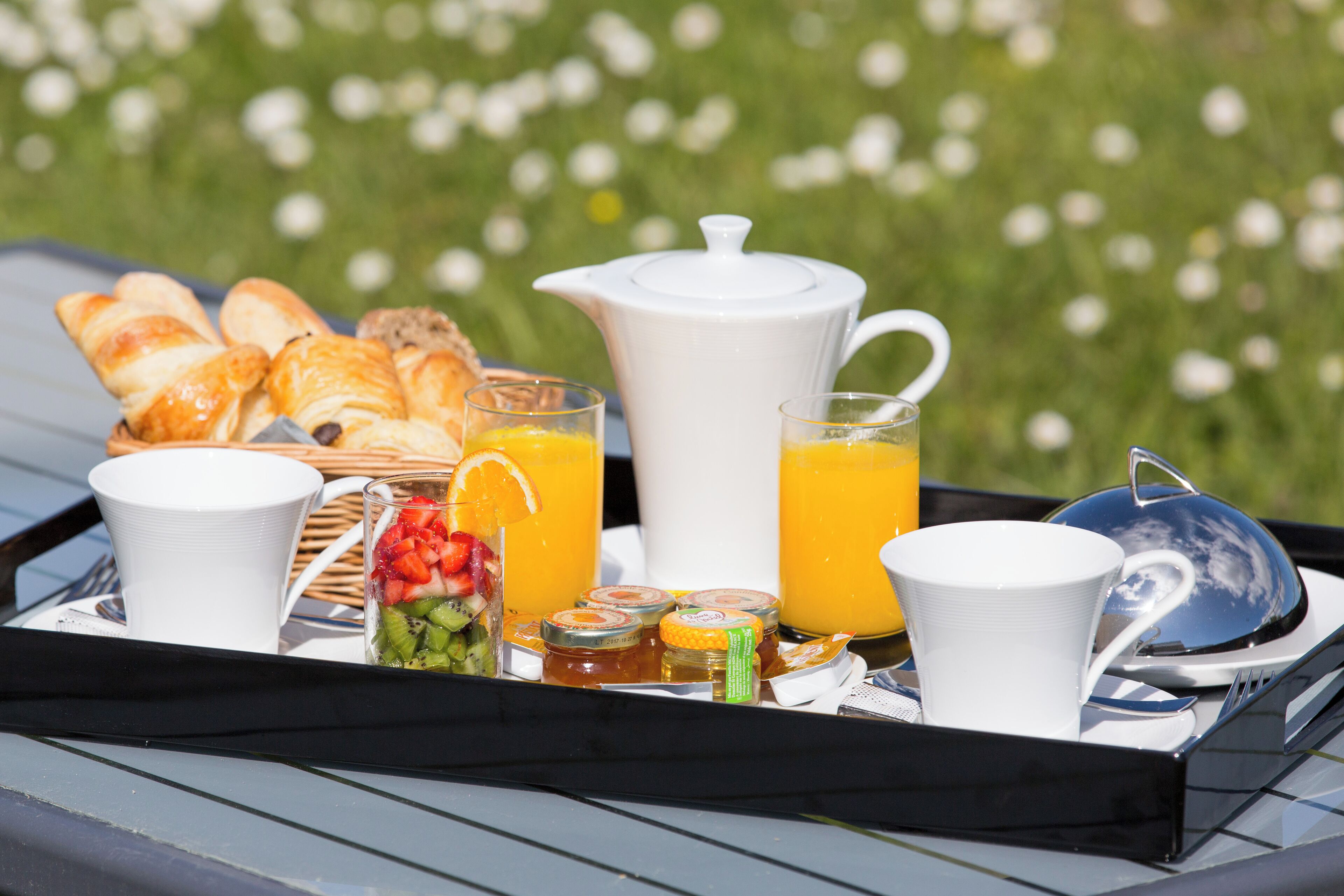 Una bandeja de desayuno con cruasanes, jugo de naranja y una tetera sobre el techo de un coche.
