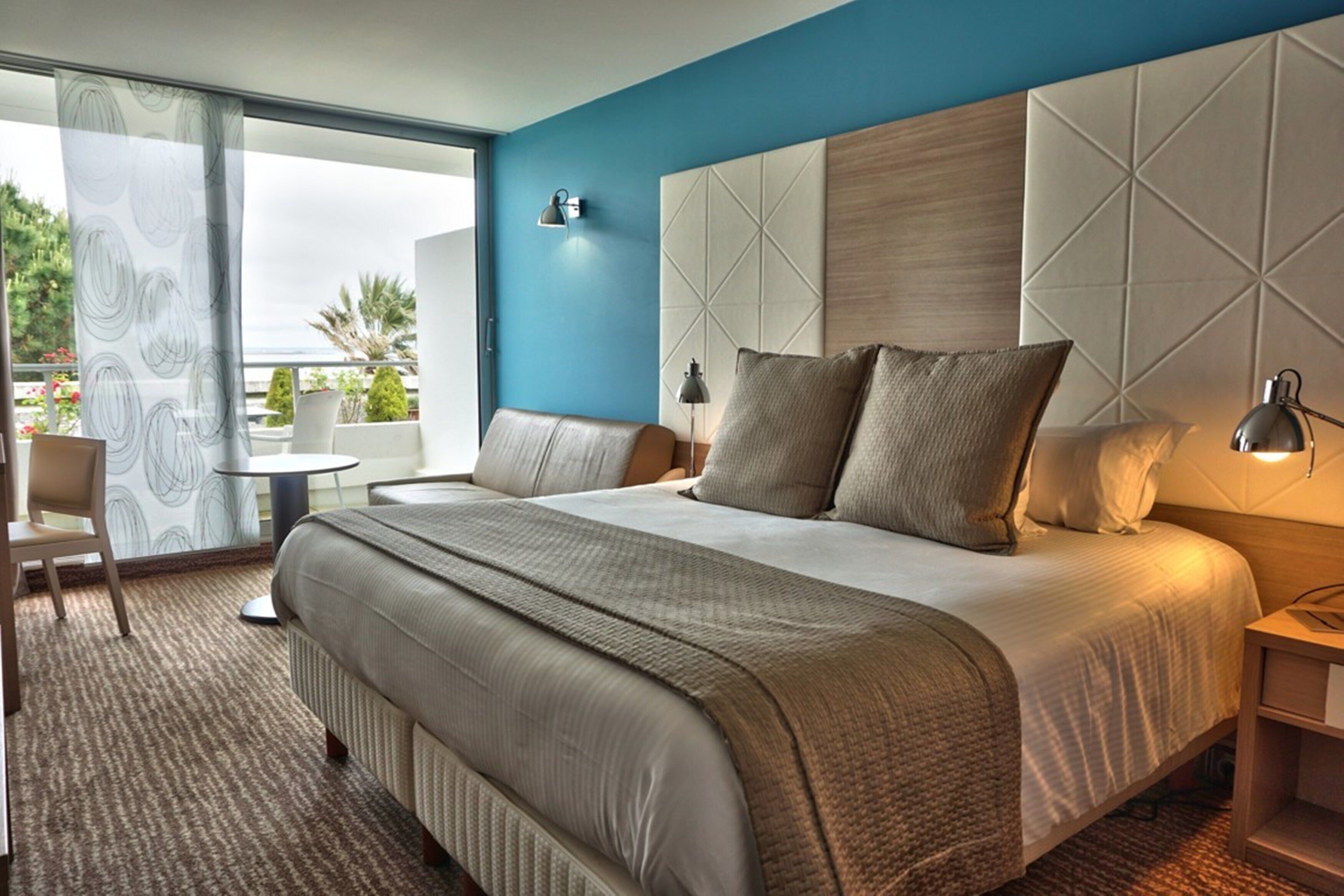 A hotel room with a large bed, a desk, a chair, a view of the outdoors, and a modern design.