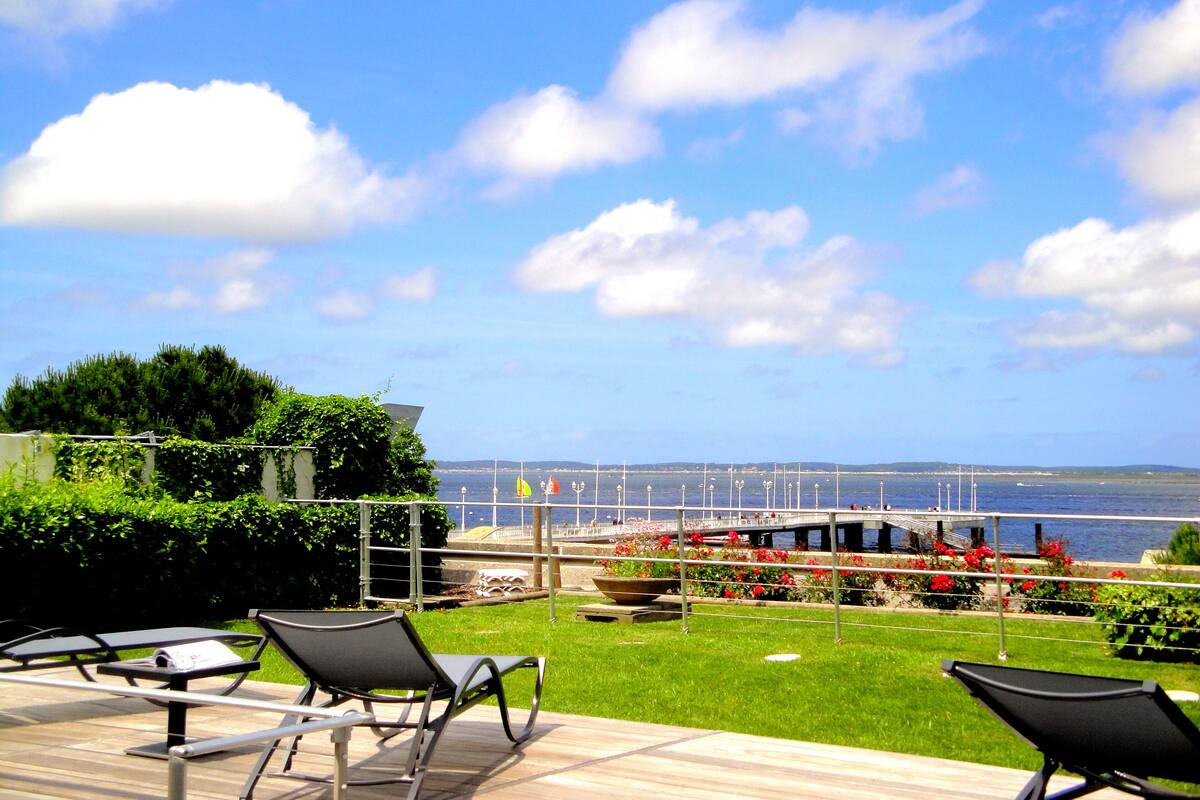 A terrace with lounge chairs, a view of the sea, and a flower bed.