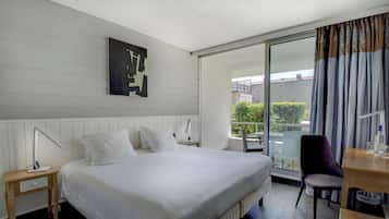 A hotel room with a large bed, a desk, a chair, a nightstand, a lamp, and a sliding glass door to the balcony.