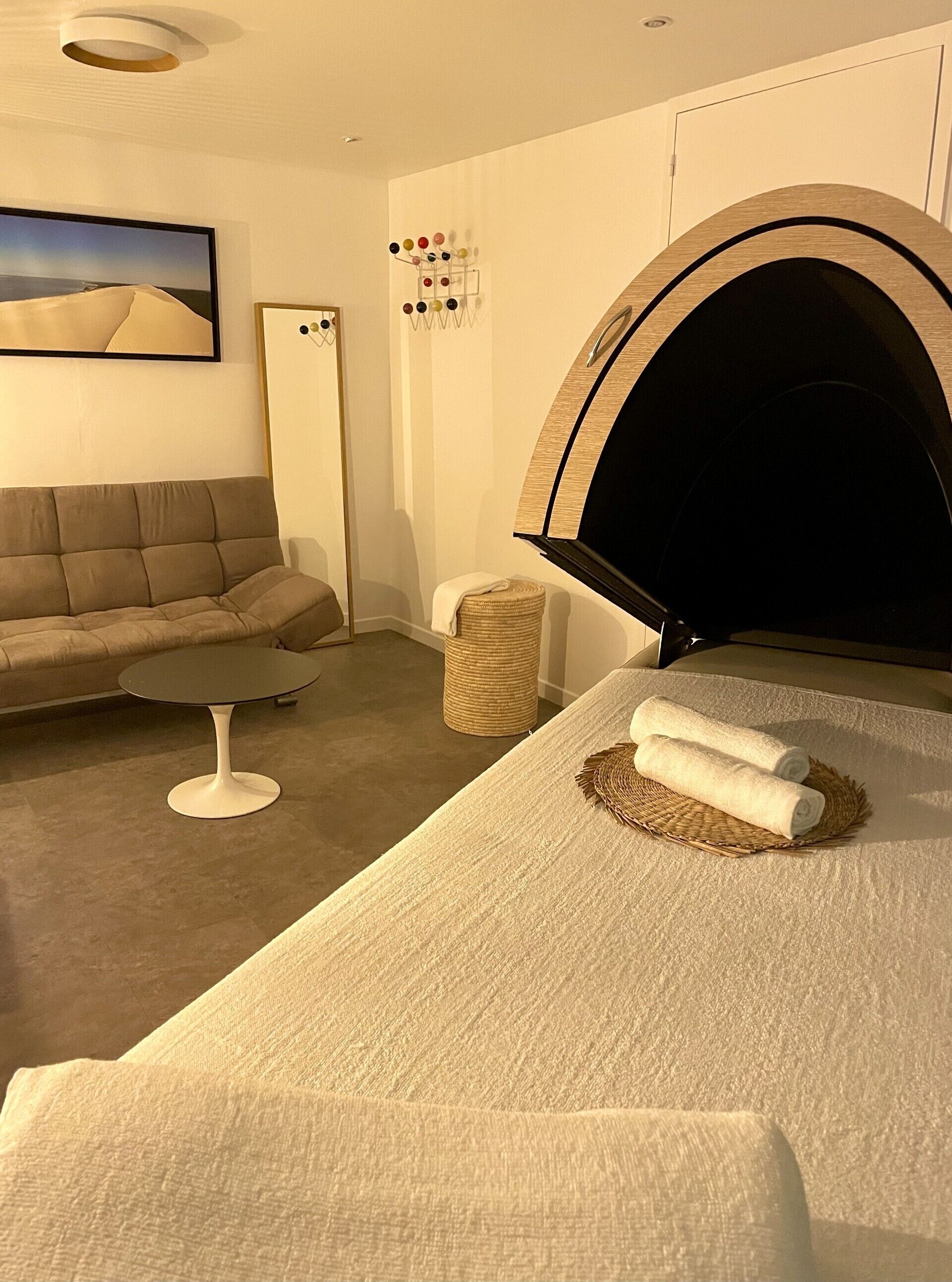 A modern bedroom with a large bed, a sofa, a small round table, and a wall-mounted TV.
