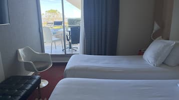 A hotel room with two beds, a desk, a chair, and a view of the outdoors.