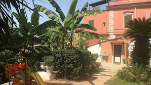 A patio area with a children's playset, including a slide and swings, surrounded by lush greenery and a building with a red facade. - Vatican Garden House (Rome)