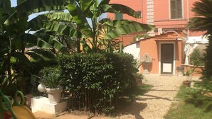A courtyard with a children's play area, including a slide, surrounded by large banana plants and potted plants. - Vatican Garden House (Rome)