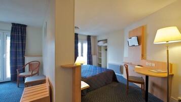 Habitación de hotel con cama, escritorio, silla, lámpara, televisión y ventana con cortinas.
