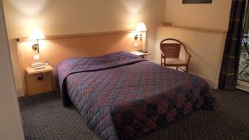 Habitación de hotel con cama, dos lámparas de noche, una silla, mesita de noche con teléfono y un cuadro en la pared.