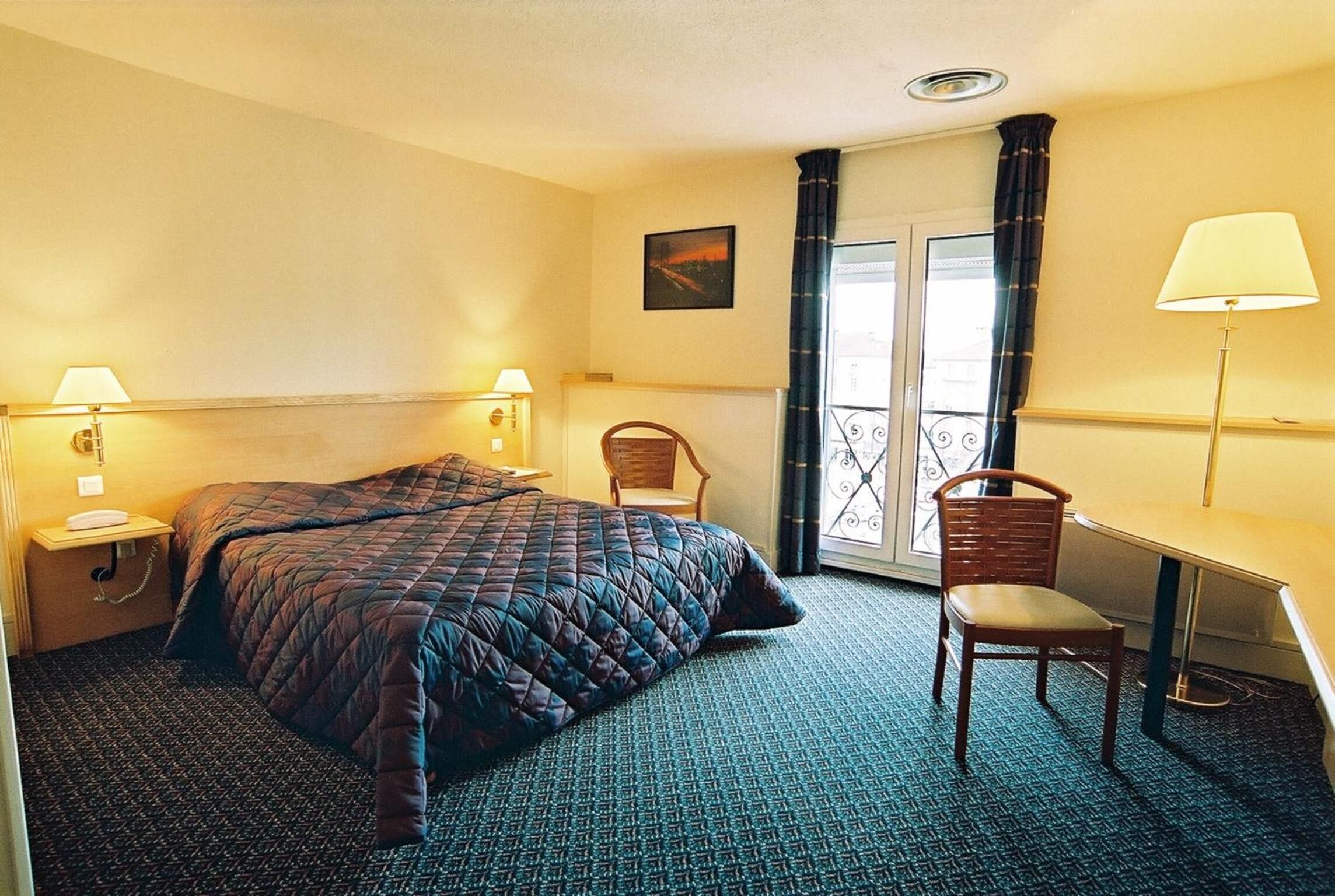 A hotel room with a bed, two chairs, a desk, and a window with curtains.