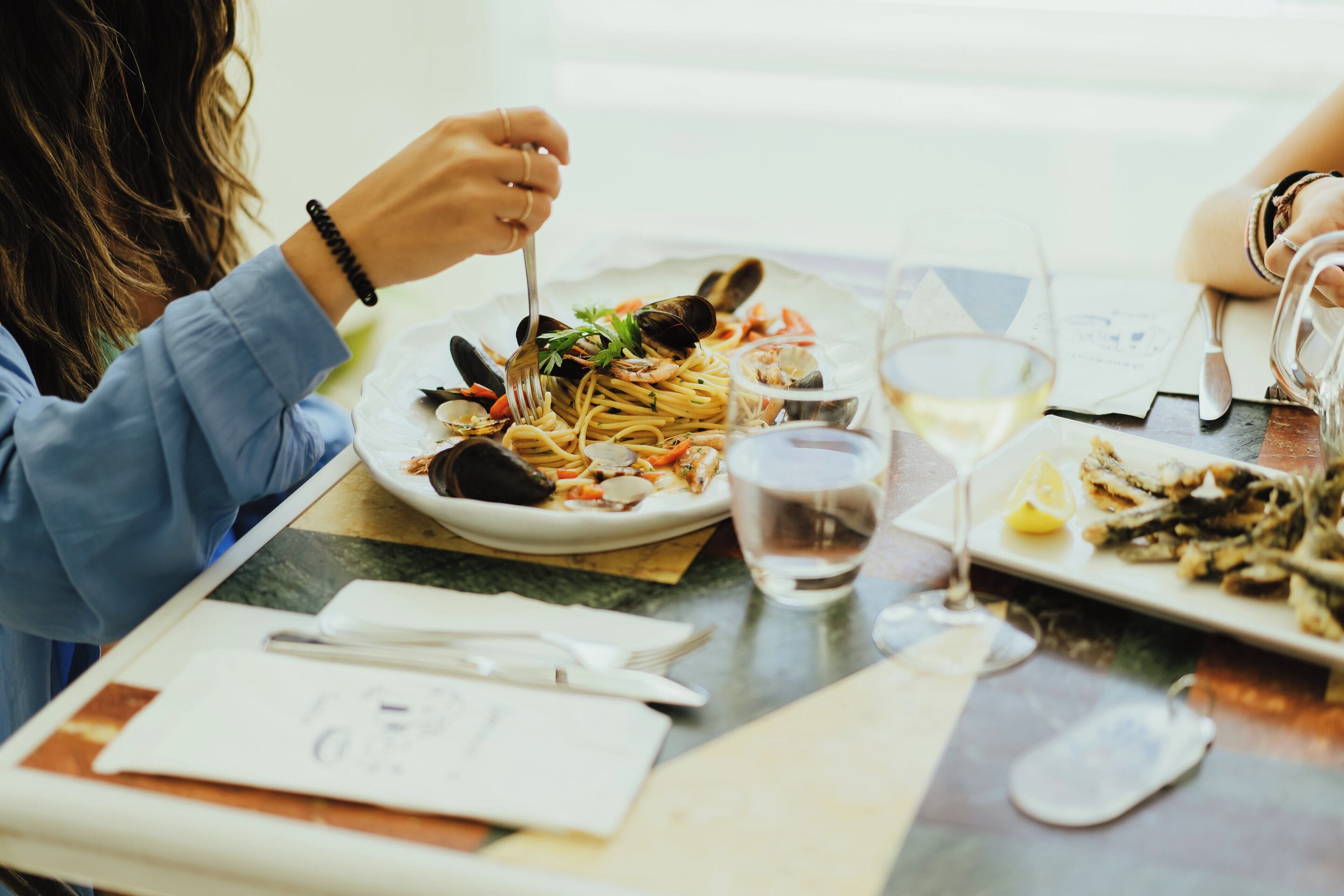 A dining table with plates of seafood pasta, a glass of water, and a wine glass.
