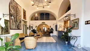 A spacious lobby with a blue carpet, wicker furniture, and a chandelier. - Hotel Terme Zi' Carmela (Forio)