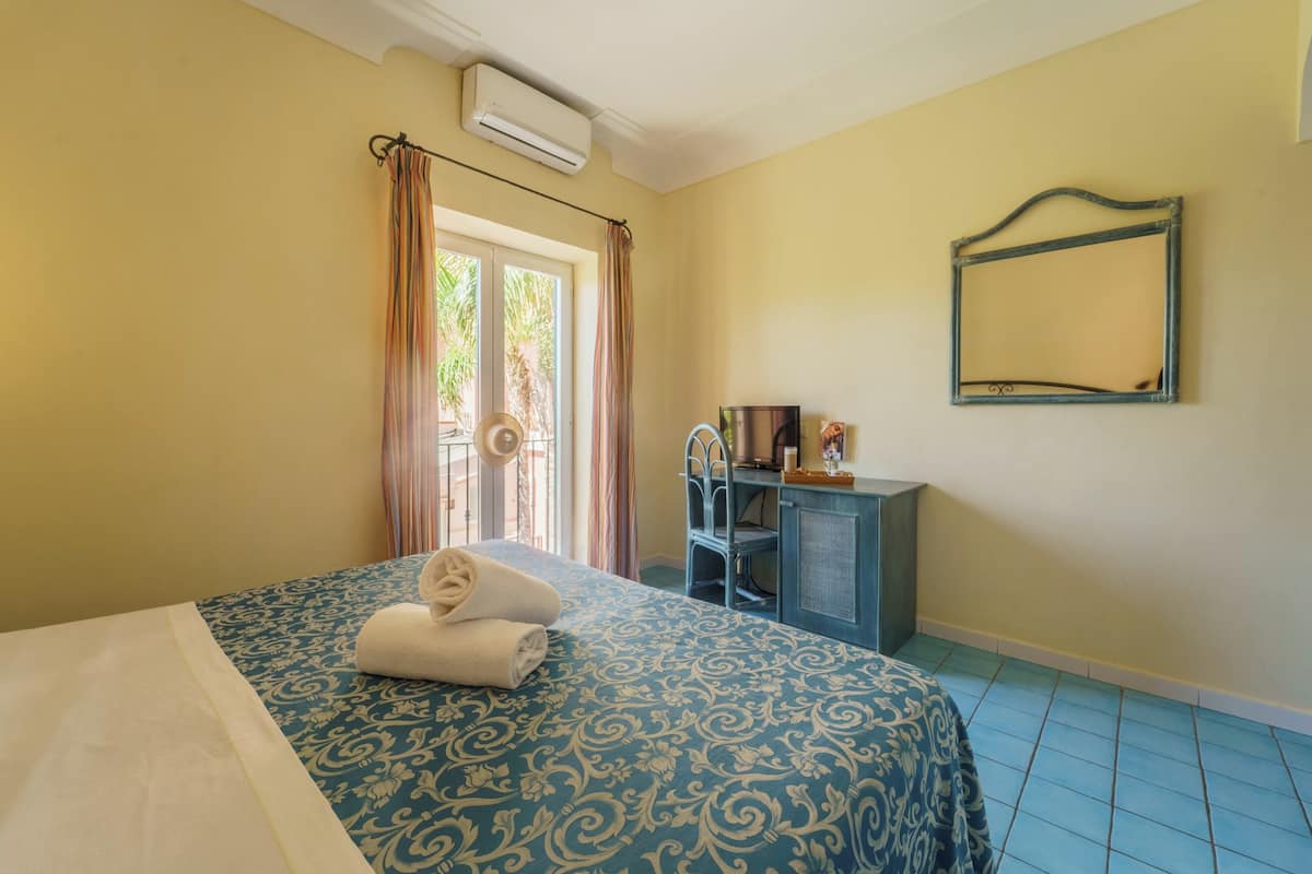 A hotel room with a bed, a desk, a chair, a mirror, and a window with curtains.