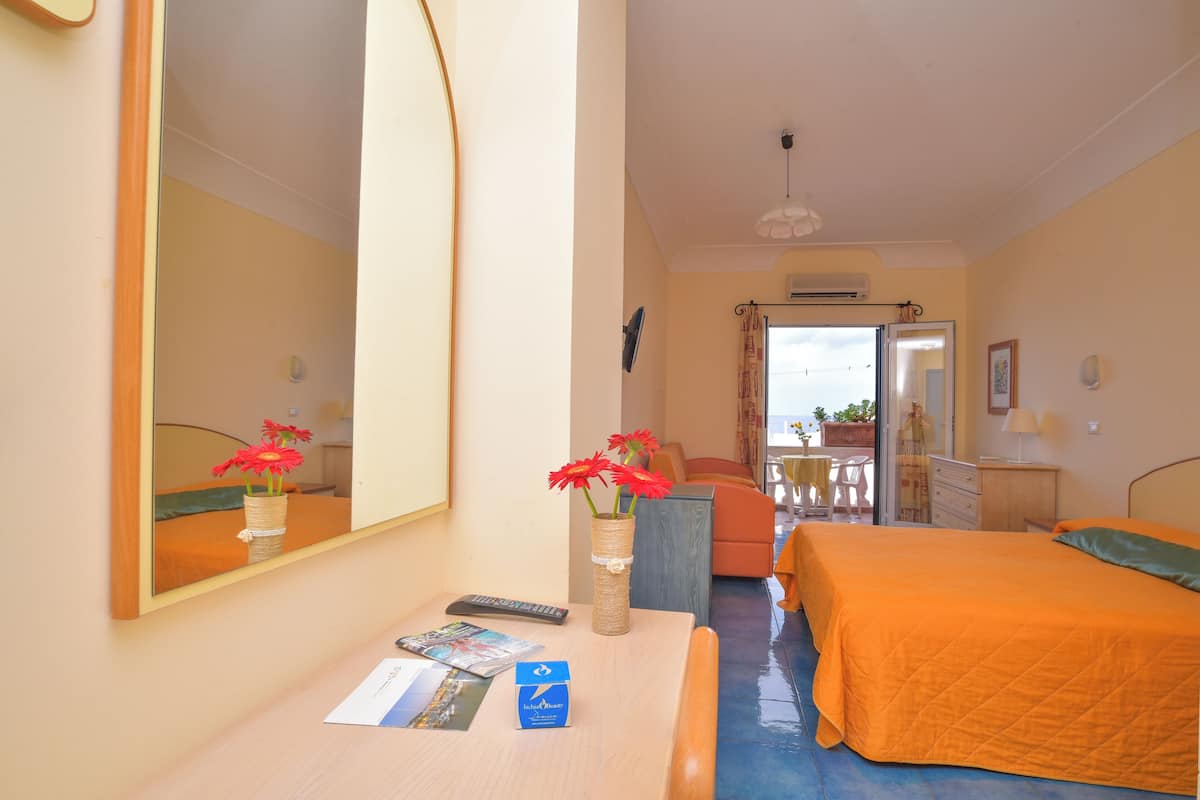 A hotel room with a bed, a desk with a vase of flowers, a mirror, and a balcony with a table and chairs.
