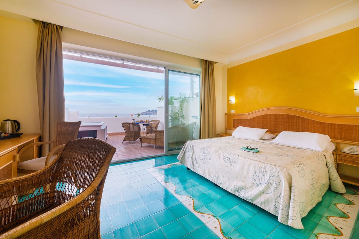 A hotel room with a bed, a chair, a table, and a view of the outdoors.
