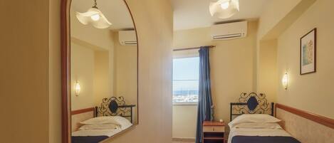 Habitación de hotel con dos camas, un espejo grande, una ventana con vistas y un equipo de aire acondicionado.