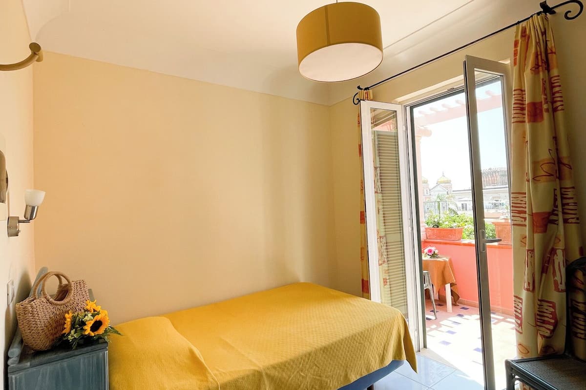 A room with a bed, a desk, a telephone, and a window with a view of the outside.