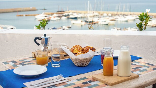 A breakfast setup with pastries, orange juice, and milk on a table with a view of a marina. - Hotel Terme Zi' Carmela (Forio)