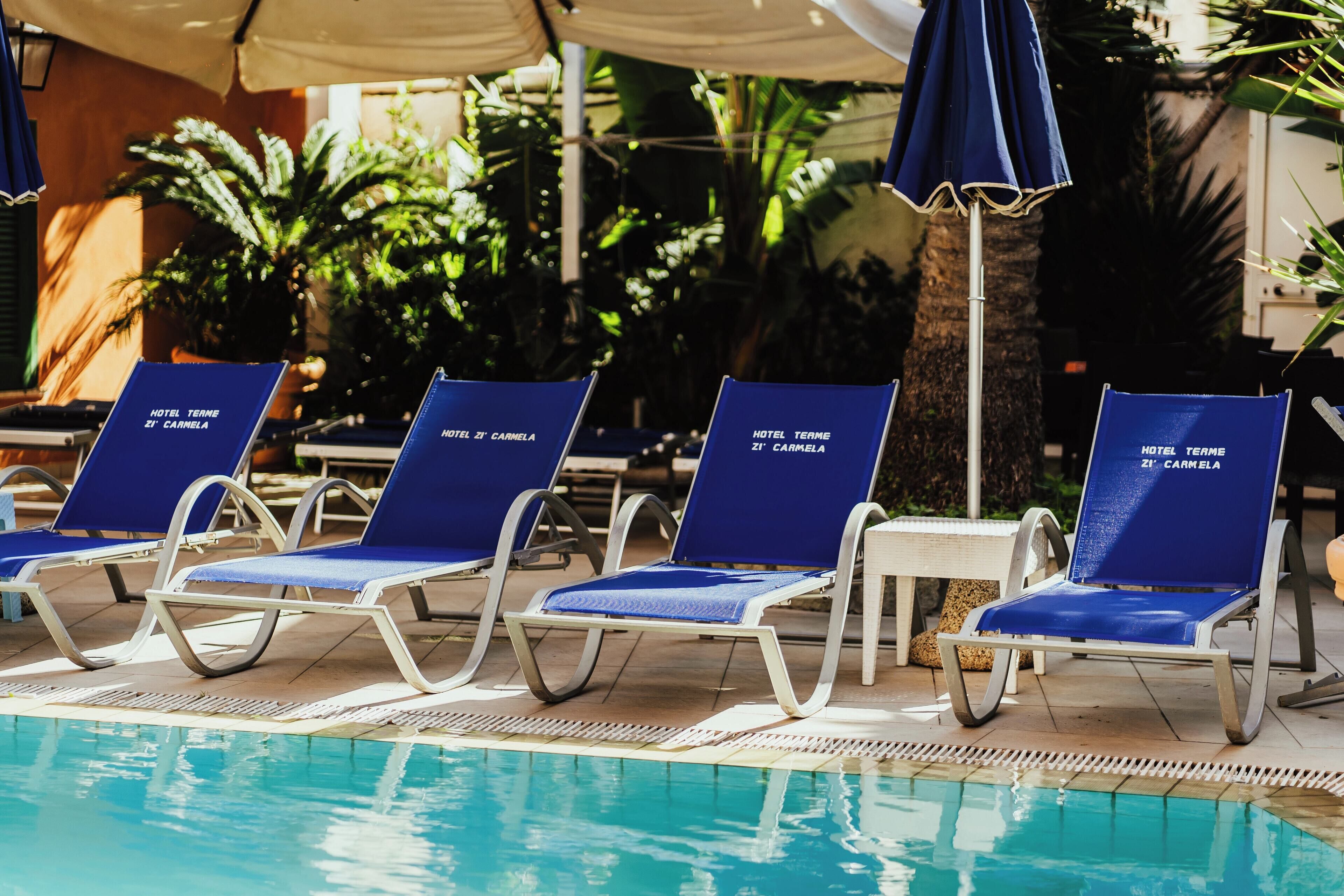 A poolside area with lounge chairs labeled "HOTEL TERME 21 - CARMELA" and a palm tree in the background.