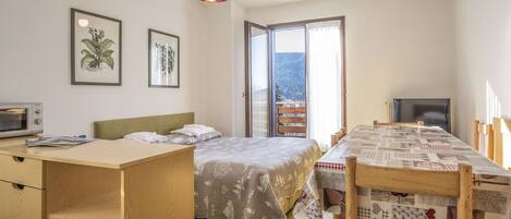 Un dormitorio con cama, escritorio, mesa de comedor y televisor.