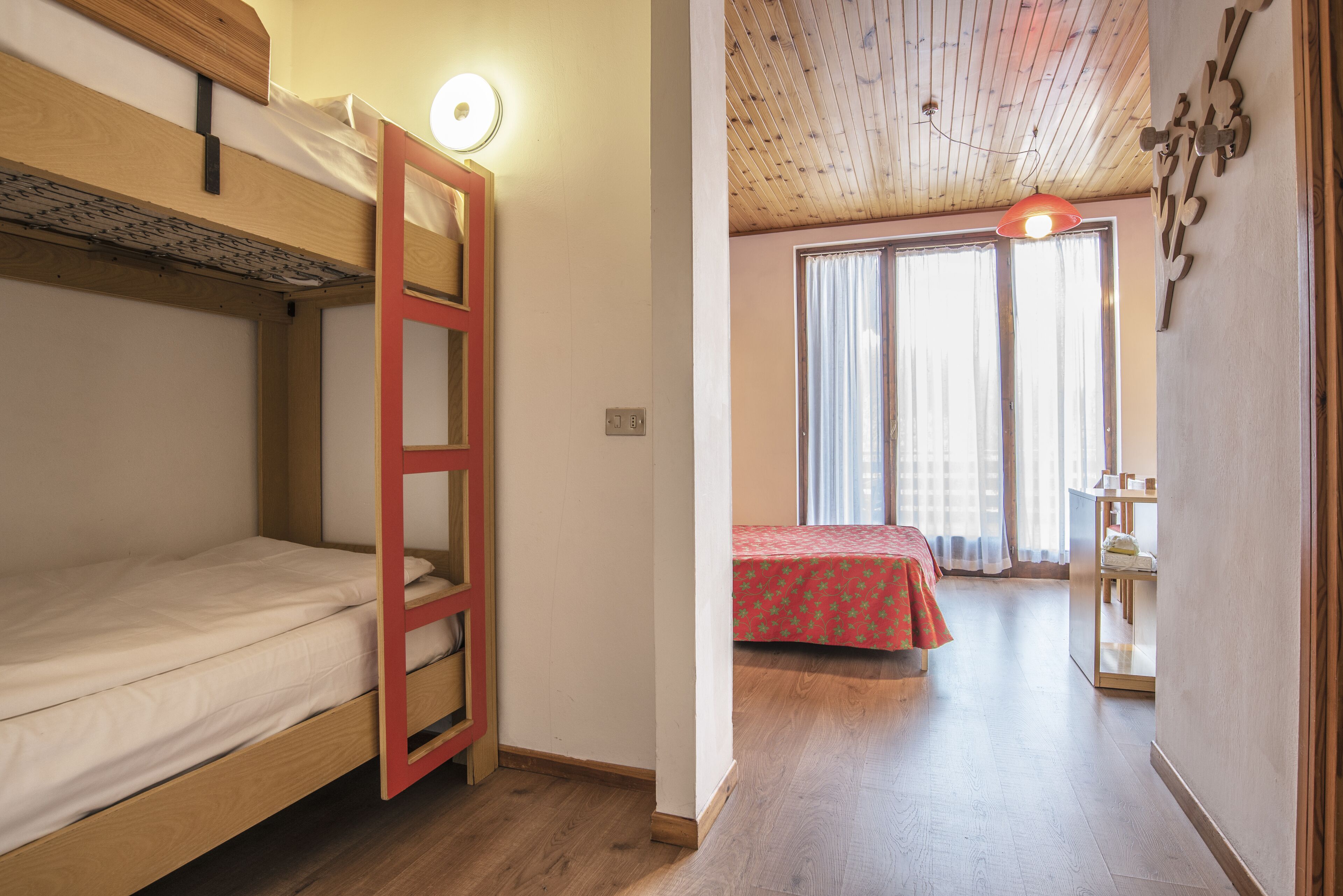 A room with a bunk bed, a desk, and a window with curtains.