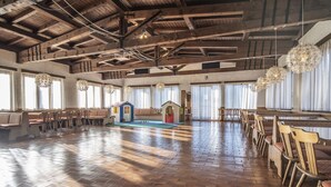 Un amplio salón con piso de madera, hileras de sillas de madera y una pequeña zona de juegos con una casita modelo.