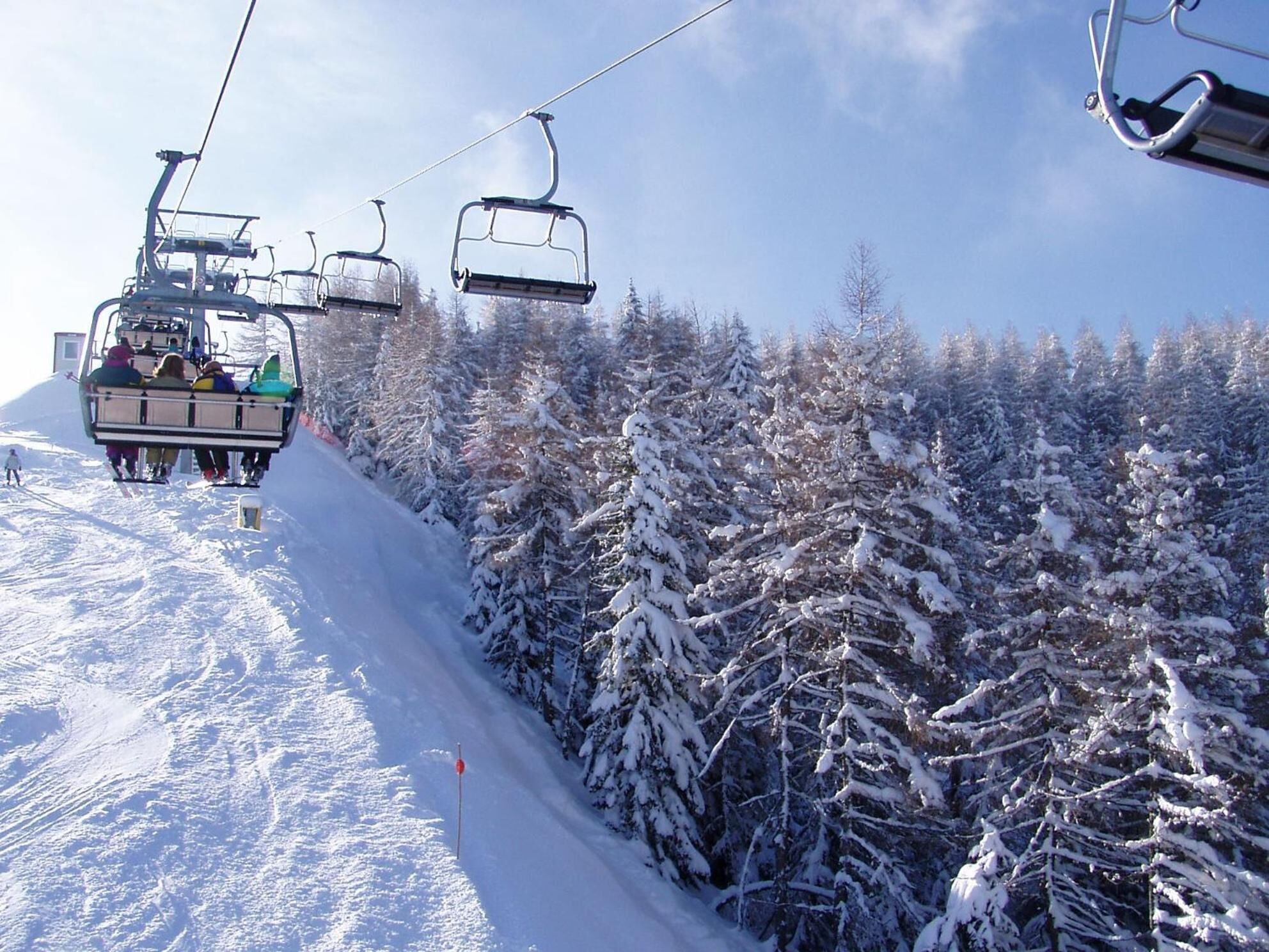 A ski lift with passengers ascending a snowy slope, surrounded by snow-covered trees.