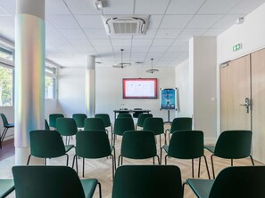 Un salón de conferencias con sillas verdes, una pantalla de proyector, una pizarra y una puerta de madera.