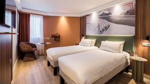 Habitación de hotel con dos camas, televisión, una mesita, una silla y un estante en la pared.